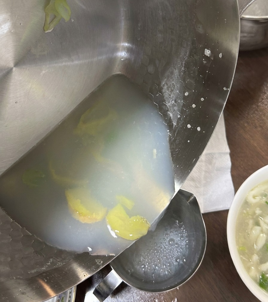 Bouillon de palourdes blanc et laiteux versé dune poêle vers un récipient, laissant derrière lui les sédiments.
