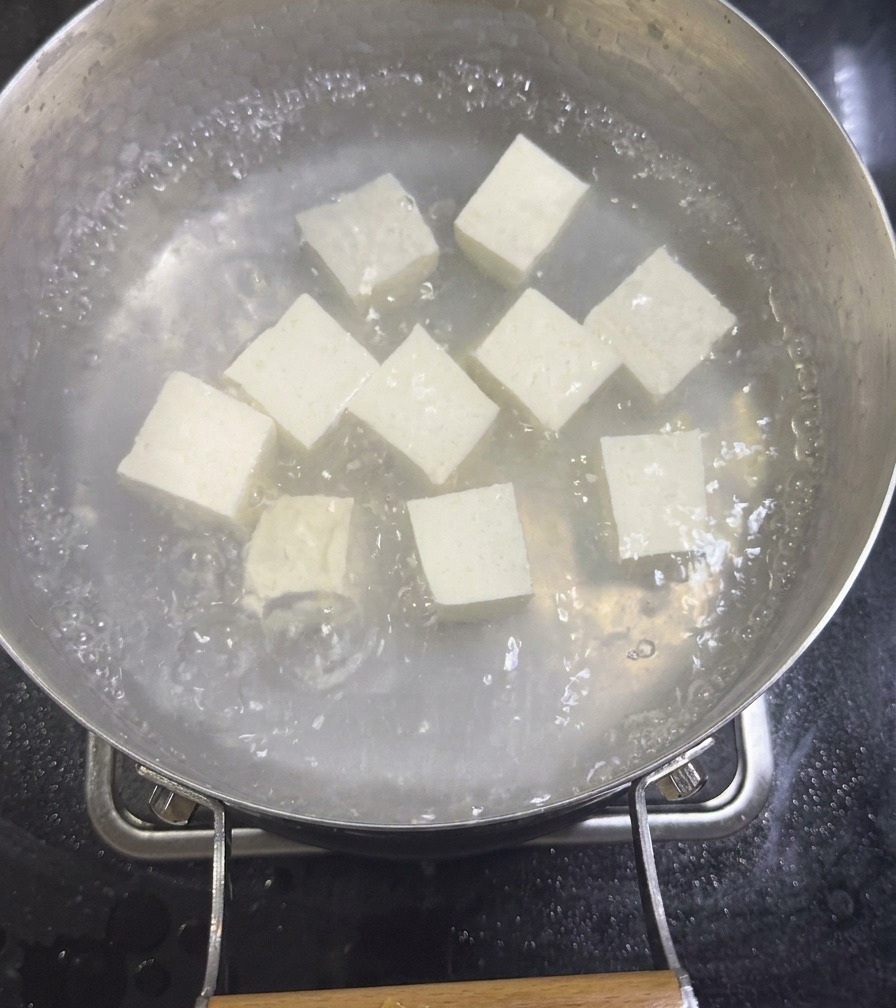 Dés de tofu soyeux blanc mijotant dans une casserole de bouillon de palourdes dilué sur une cuisinière.