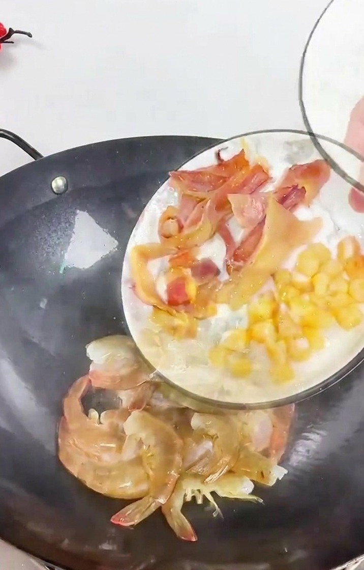 Une personne versant une assiette de calamar émincé et de noix de Saint-Jacques séchées dans un wok sombre contenant des crevettes et du gingembre.