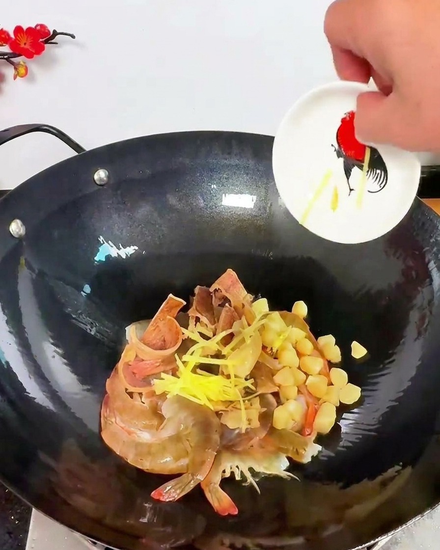 De fins bâtonnets de gingembre jaune parsemés sur un mélange de crevettes crues et de noix de Saint-Jacques dans un wok.
