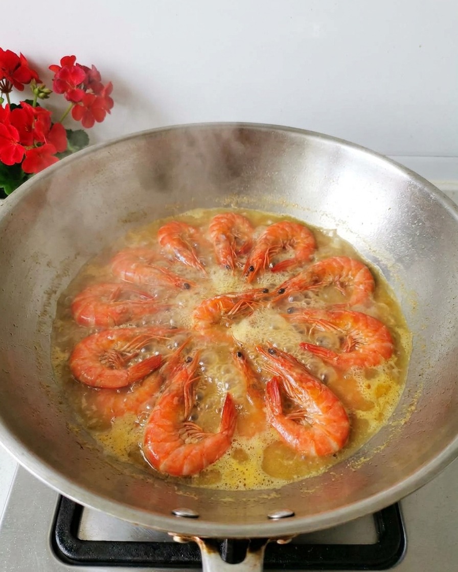 Des crevettes orange bouillant dans un bouillon clair à lintérieur dun wok en inox avec de la vapeur montante.