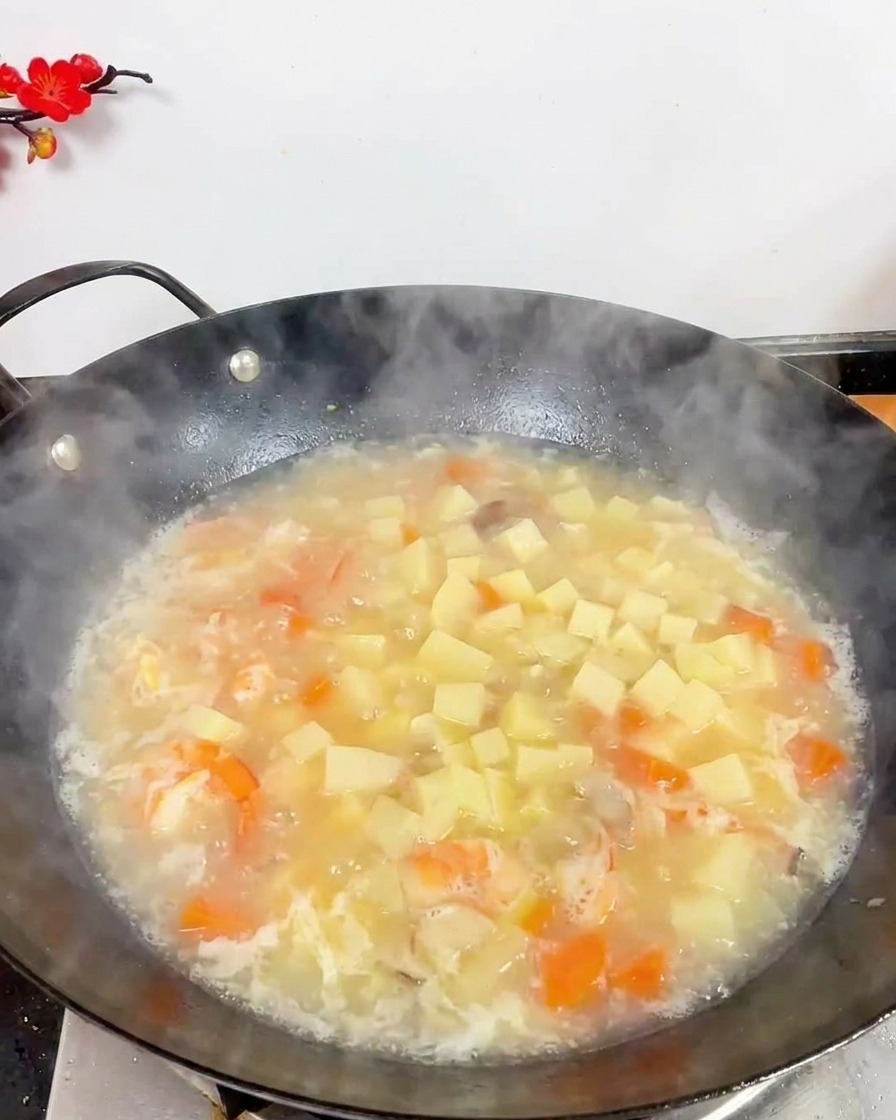 Vue de dessus dun wok rempli dune soupe blanche bouillonnante avec du tofu, des crevettes et des petits champignons bruns.