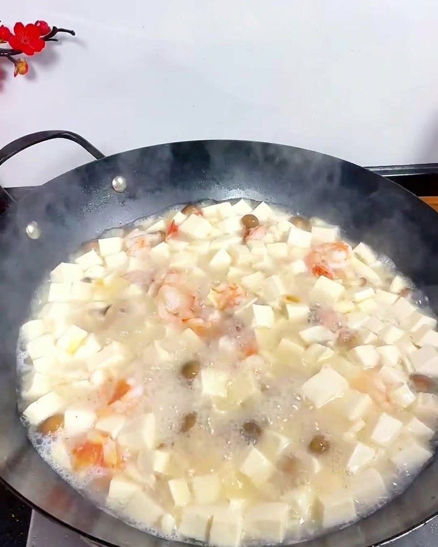 Une cuillère métallique saupoudrant du poivre blanc en poudre dans la soupe de tofu et fruits de mer en ébullition.