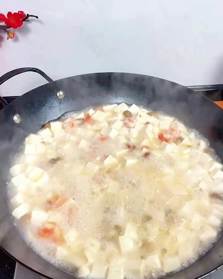 Une louche en inox versant du vinaigre sombre dans une soupe blanche bouillonnante remplie de tofu et crevettes.