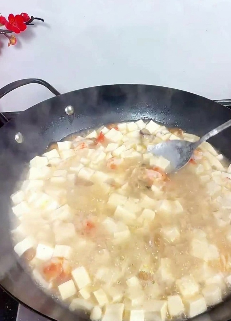 Une cuillère remuant un wok de soupe au tofu bouillonnante pour bien incorporer les assaisonnements.