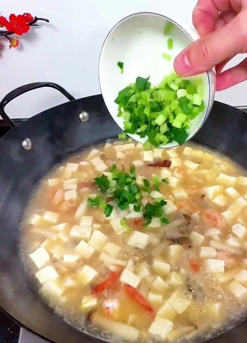 Une main penchant un bol pour verser du céleri haché et des pousses dail bien vertes dans la soupe bouillante.