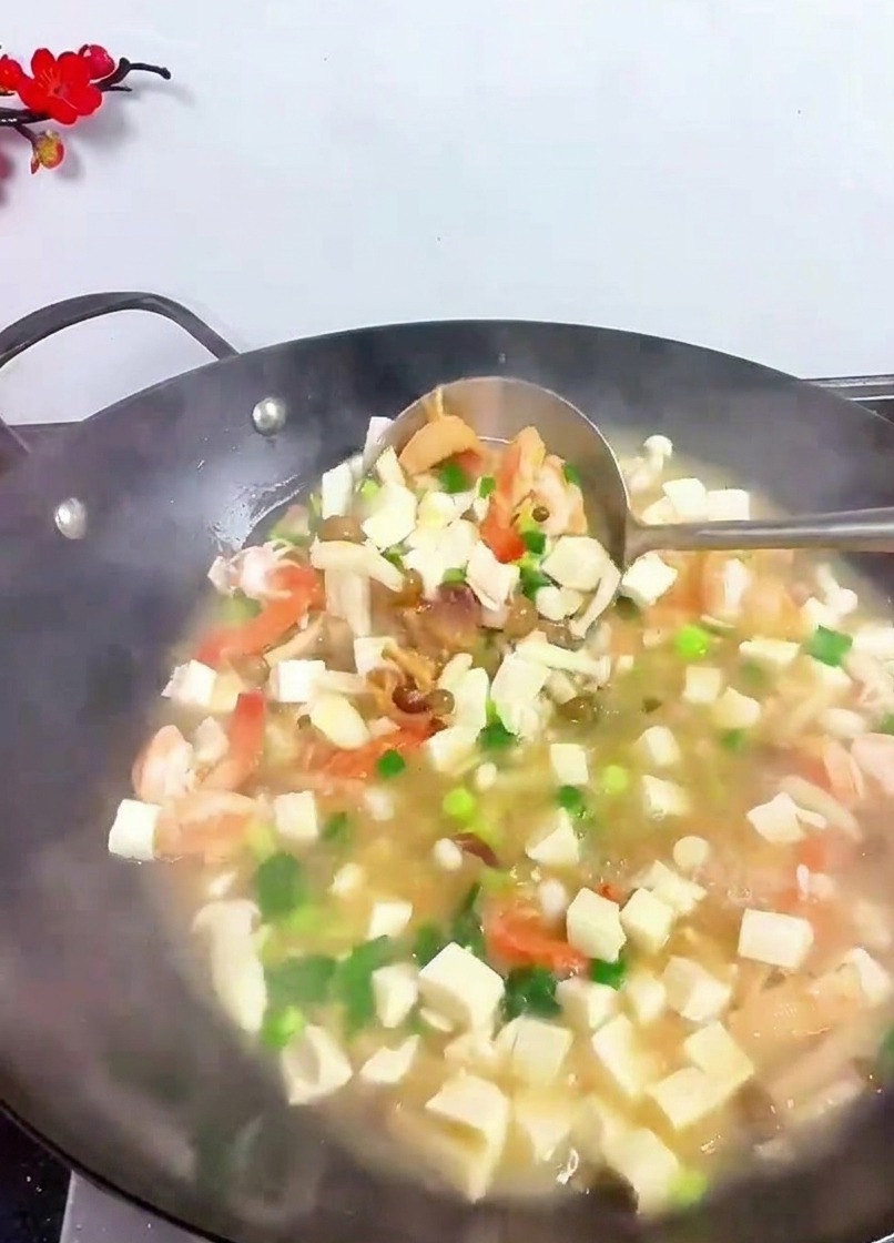 Une louche soulevant et mélangeant les dés de tofu, les crevettes et les herbes vertes dans un wok fumant.
