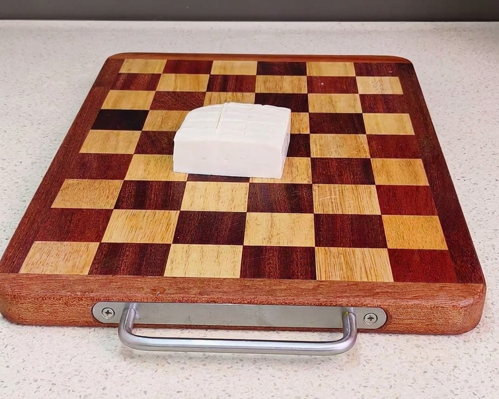 Un bloc de tofu blanc frais coupé en cubes uniformes sur une planche à découper en bois quadrillée.