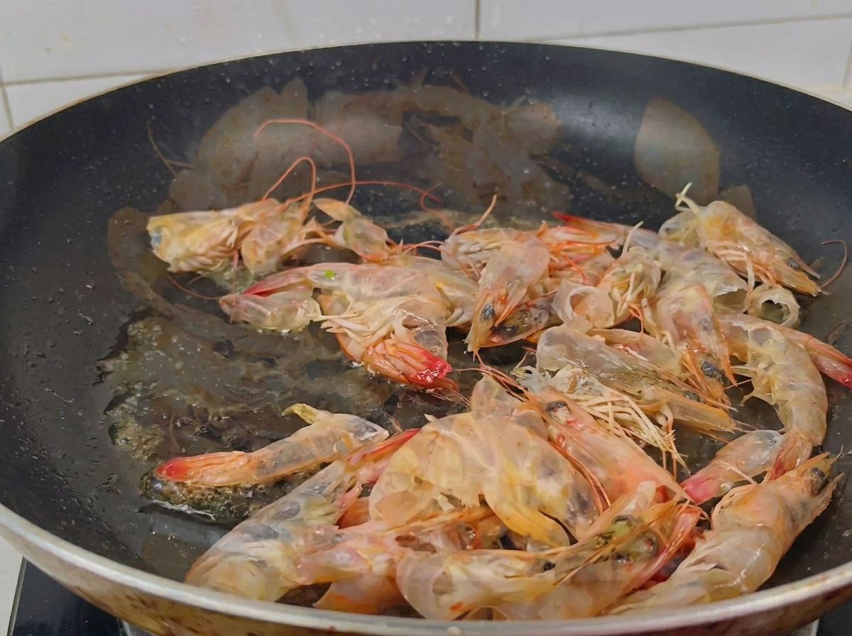Une poêle noire remplie de carapaces de crevettes translucides devenant orange vif sous leffet de la chaleur.