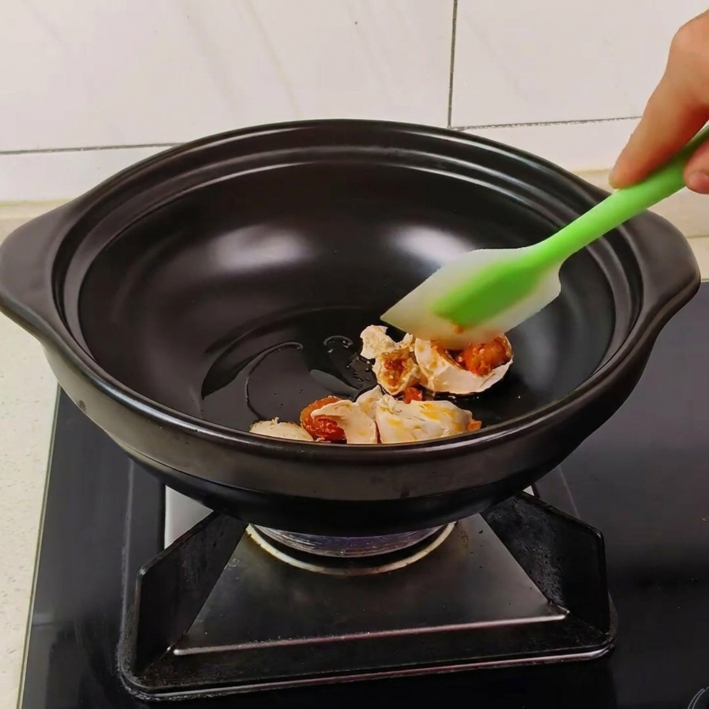 Une spatule verte remuant des morceaux dœuf de cane salé dans une marmite noire jusquà ce quils moussent.