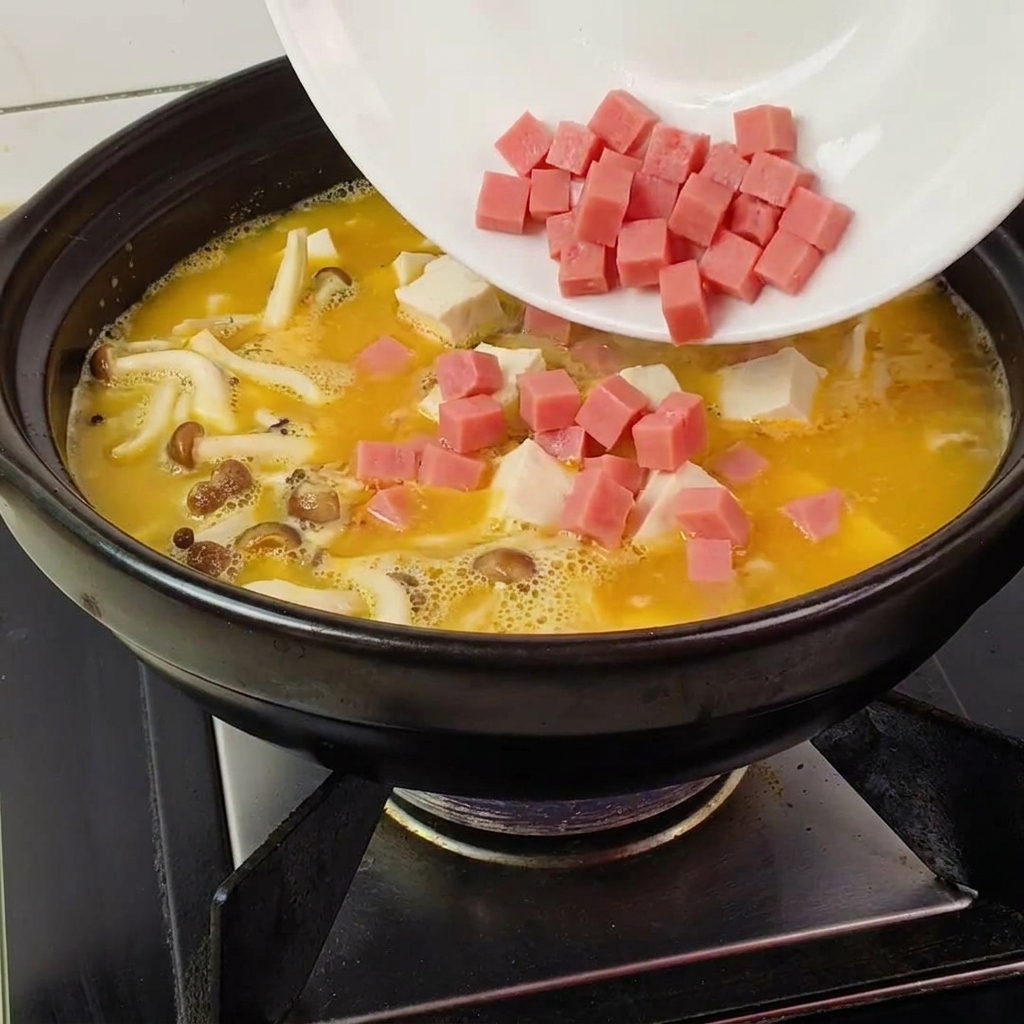 Dés de jambon versés dune assiette blanche dans une marmite noire remplie de bouillon, champignons et tofu.
