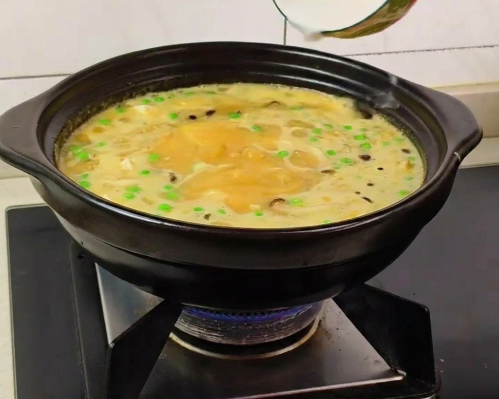 Une main versant un mélange deau et de fécule dans une soupe bouillonnante dans une marmite noire.