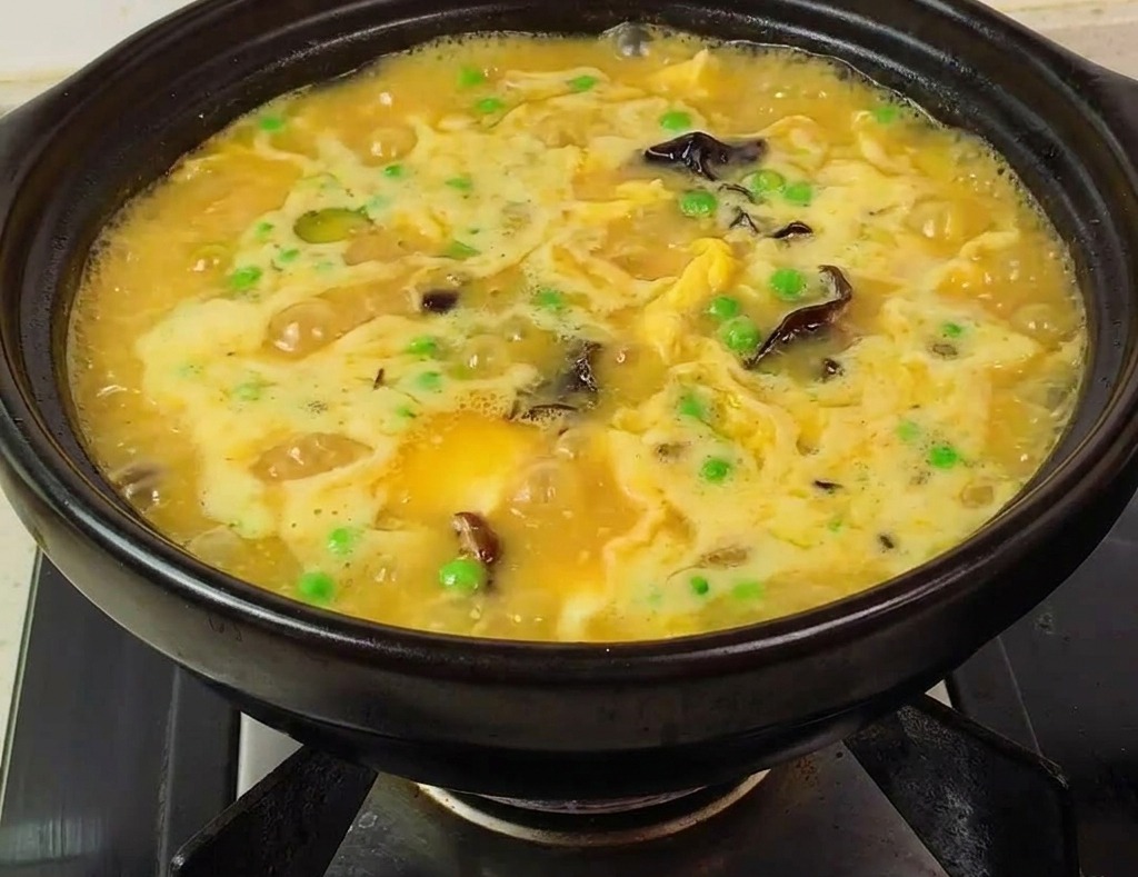 Une marmite en terre cuite remplie dune soupe jaune épaisse et bouillonnante avec crevettes et petits pois.