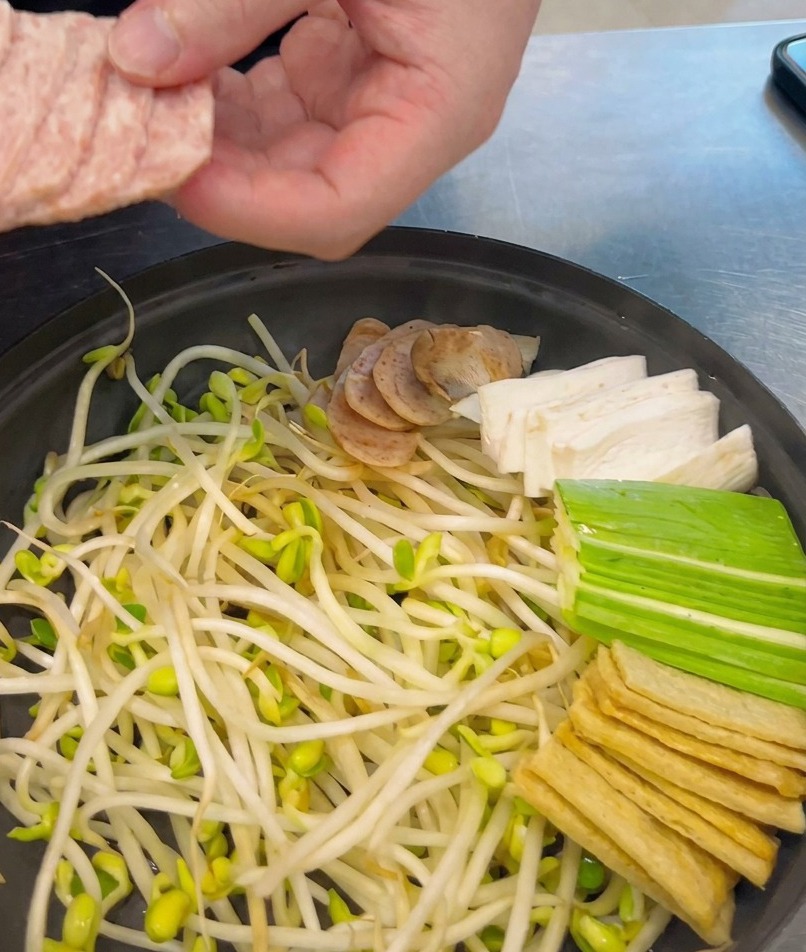 Une main disposant des tranches régulières de spam rose dans une marmite déjà garnie de légumes.