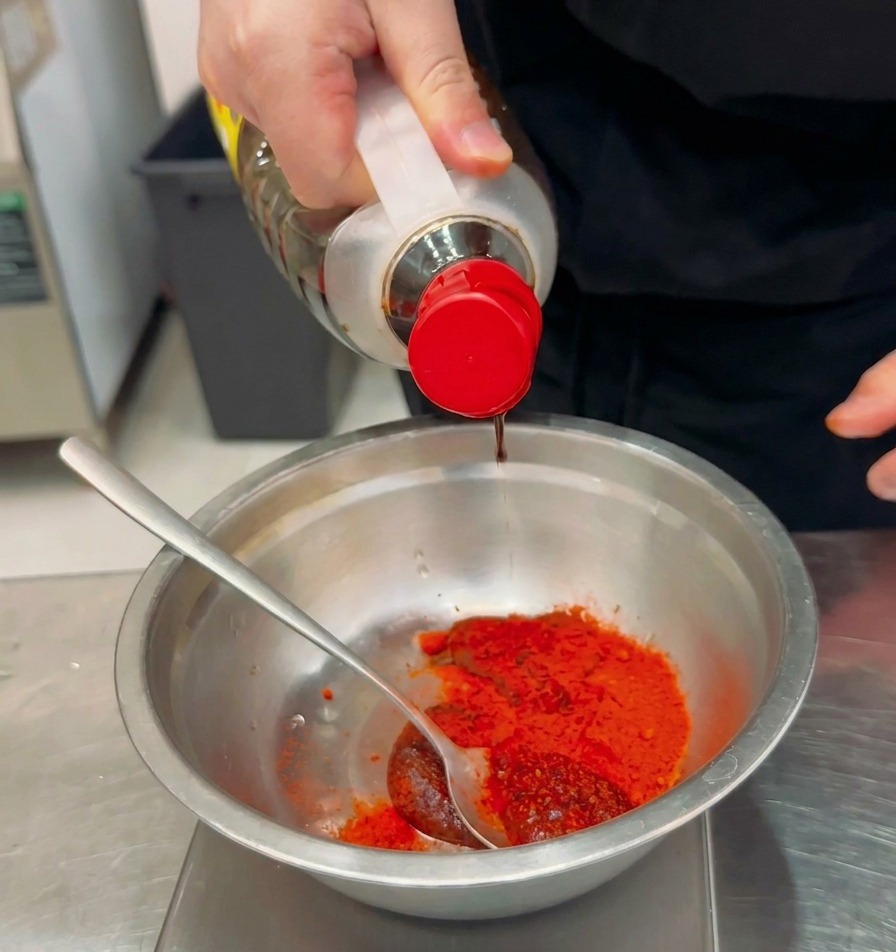 Liquide dassaisonnement versé dune bouteille dans un bol contenant de la poudre et de la pâte de piment rouge.