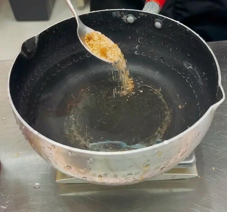 Poudre dassaisonnement versée dans une marmite deau claire pour préparer le bouillon du Budae-jjigae.
