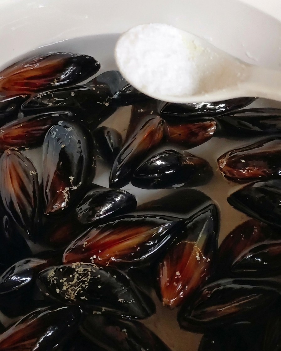Une cuillère de sel ajoutée à une casserole de moules noires immergées dans leau.