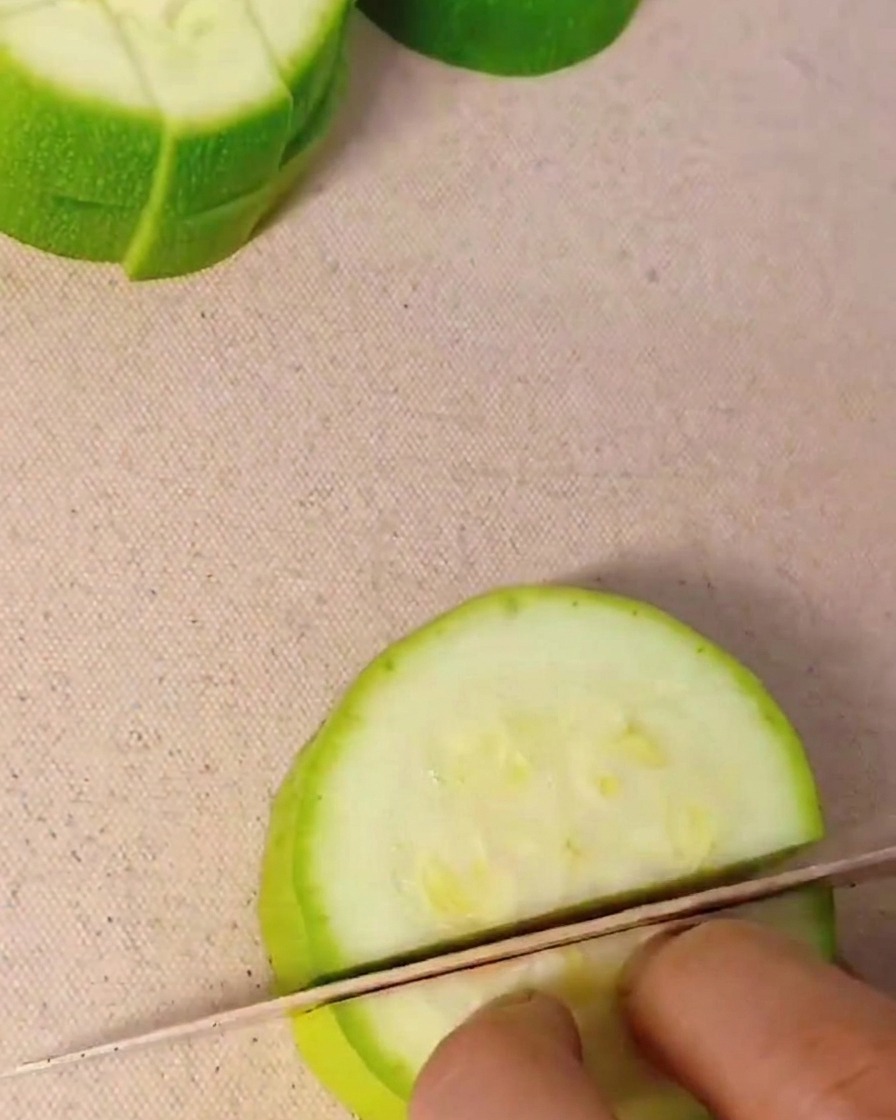 Gros plan dune main découpant une courgette verte en petits cubes sur une planche à découper.