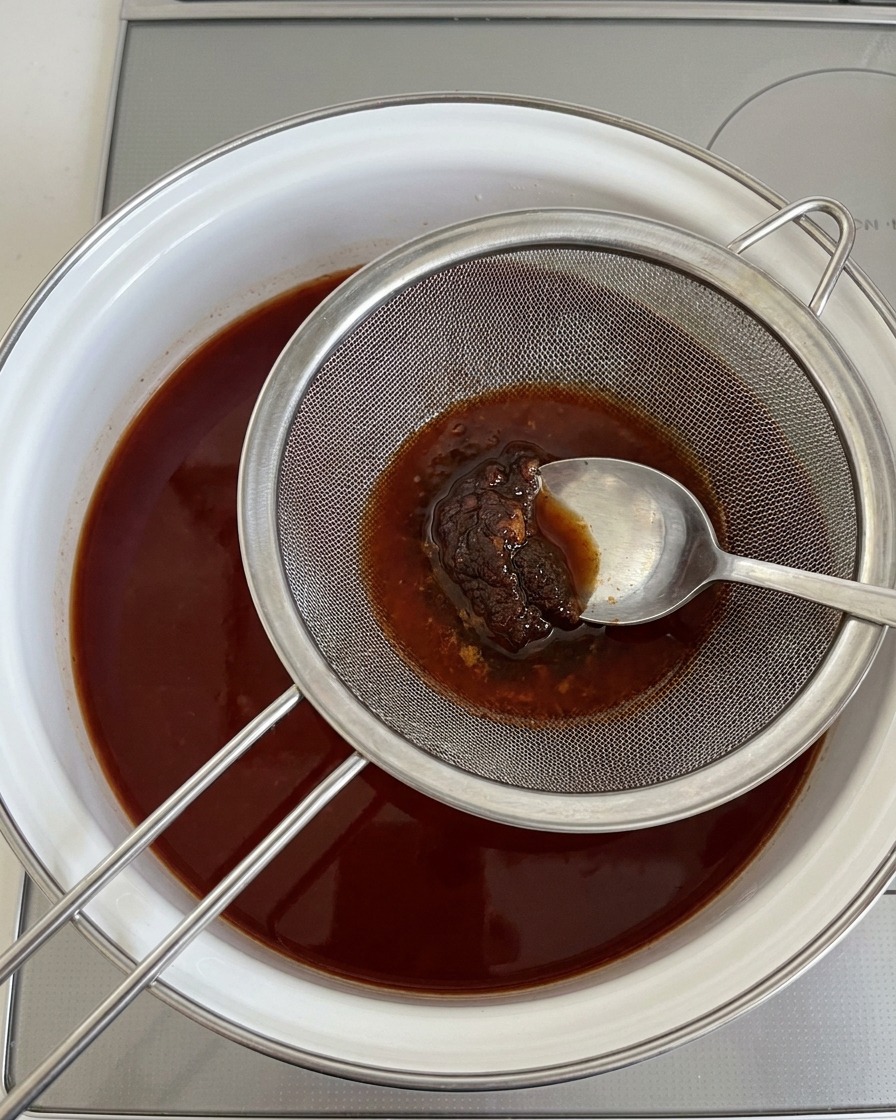 Utilisation dune cuillère pour presser la pâte de soja à travers un tamis métallique dans le bouillon.