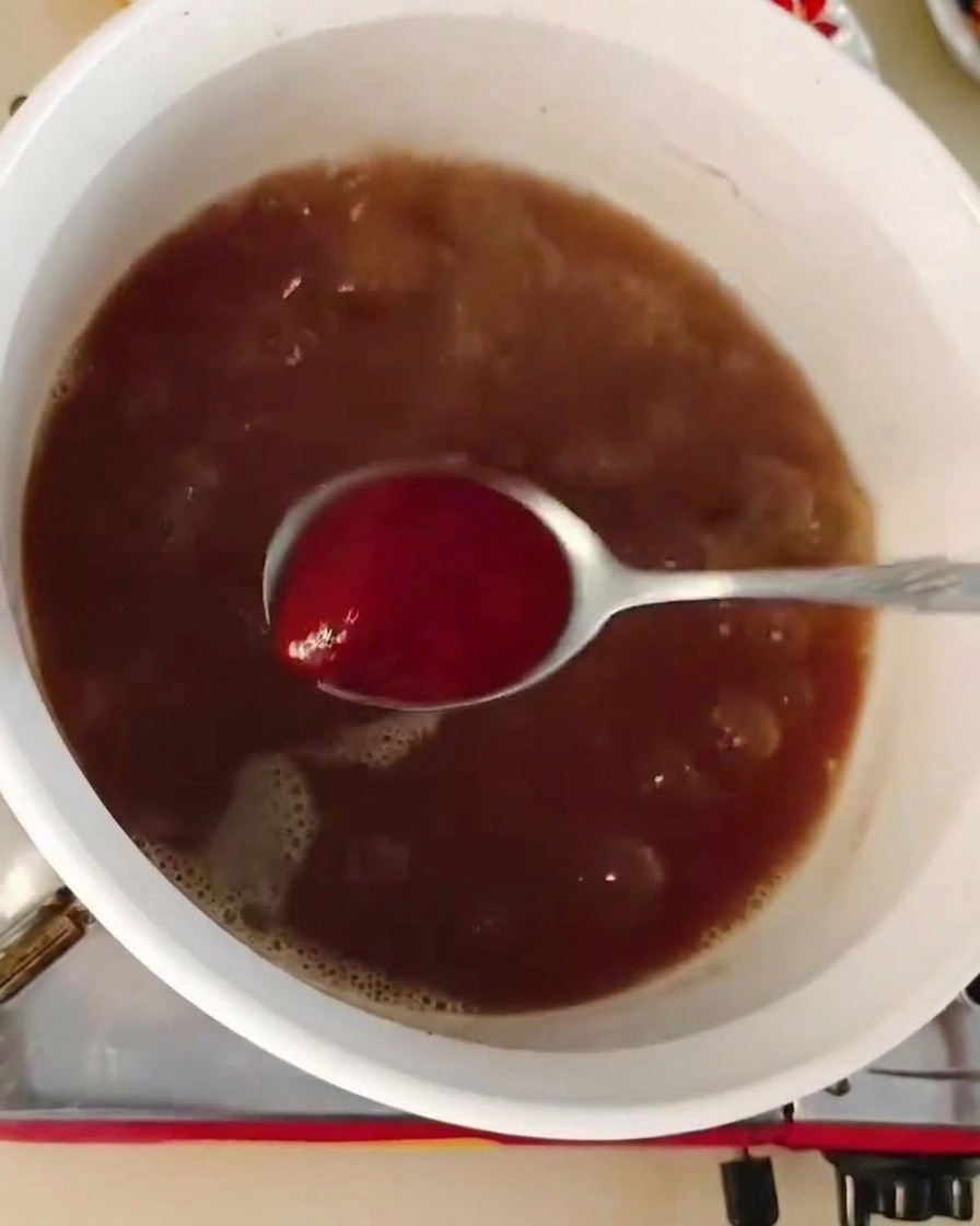 Une cuillère de pâte de piment rouge mélangée dans une marmite de bouillon brun foncé.
