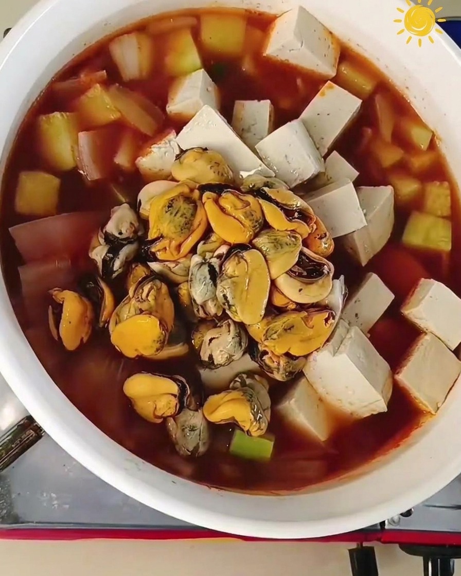 Chair de moules et grosses crevettes crues ajoutées au centre dune marmite bouillonnante avec tofu et légumes.