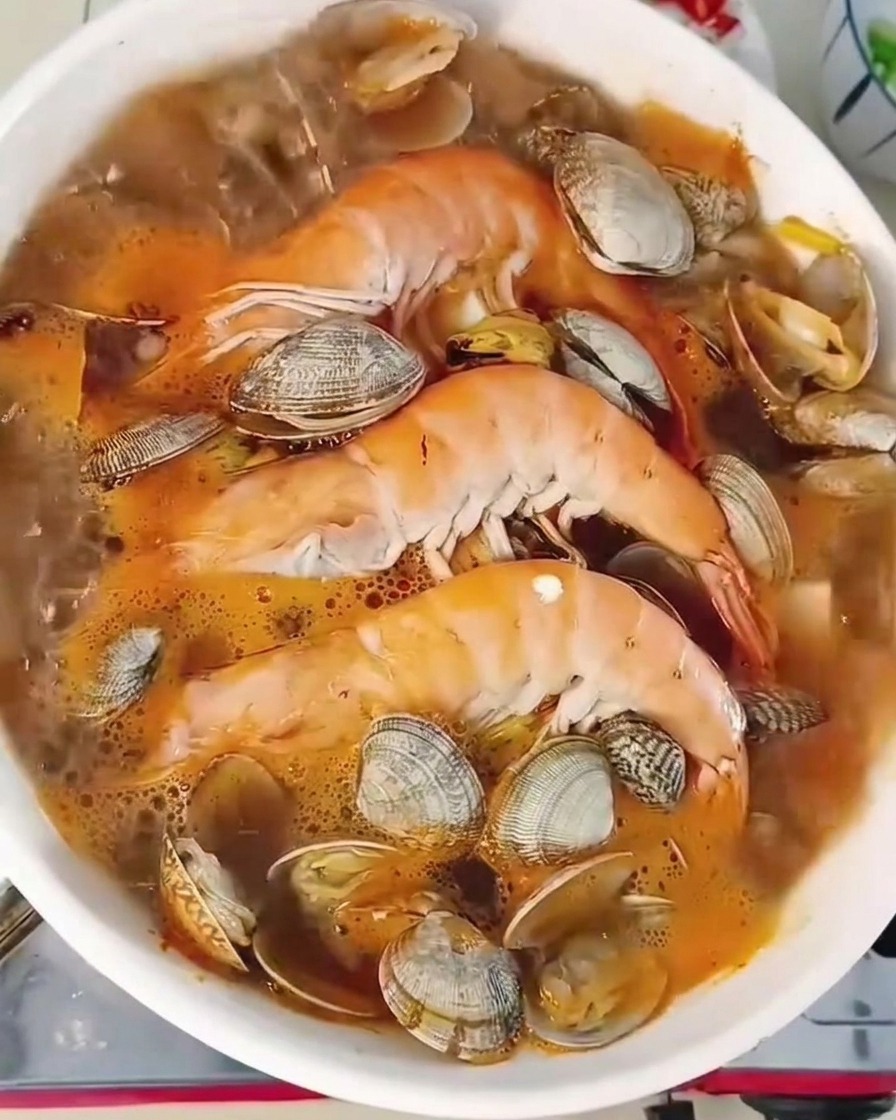 Gros plan dun ragoût bouillonnant avec crevettes et palourdes, parsemé de piments verts et doignons verts.