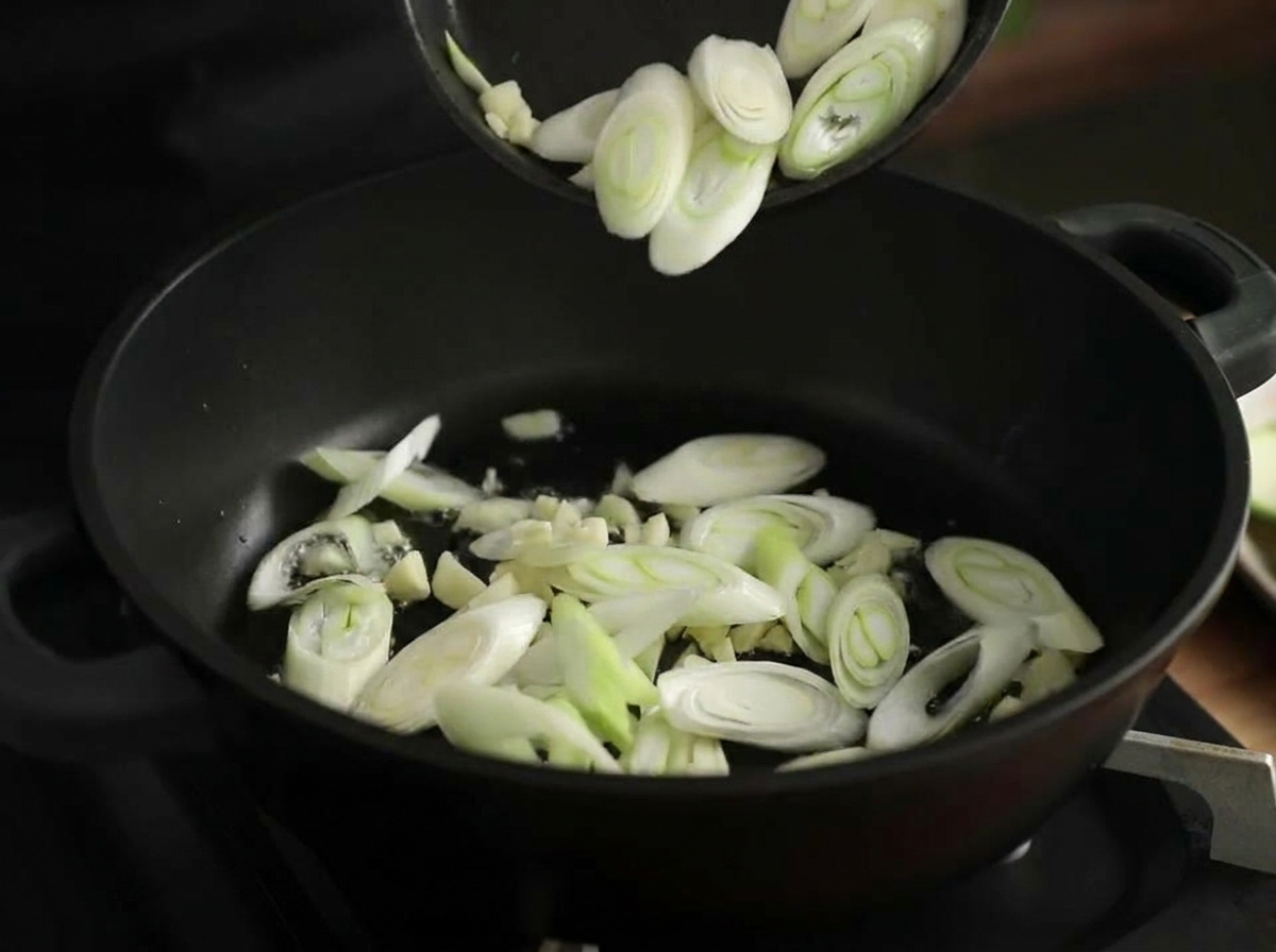 Ail haché et tranches de poireau sautant dans une marmite noire chaude avec de lhuile brillante.