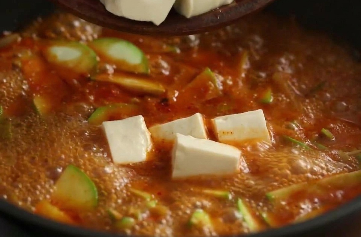 Cubes de tofu blanc tombant dun bol dans un ragoût coréen rouge vif et bouillonnant.