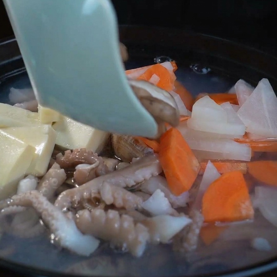 Tranches de shiitakés frais ajoutées à la soupe bouillante aux côtés du tofu et des légumes.