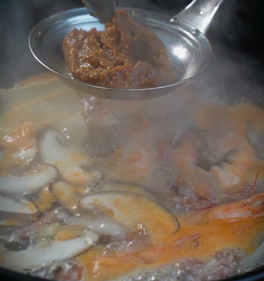 Une dose de pâte de soja brune épaisse dans un tamis métallique au-dessus de la soupe bouillante.