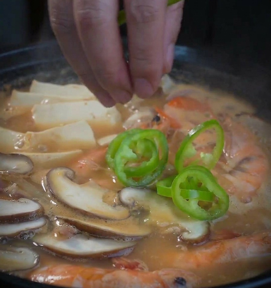 Rondelles de poivron vert ajoutées à la main dans la soupe de soja aux fruits de mer.