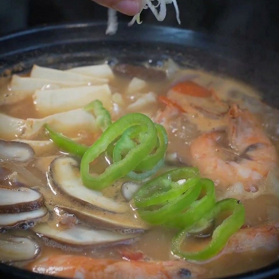 Une main parsemant un mélange doignons blancs et verts ciselés sur la soupe terminée.