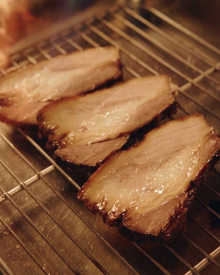 Un chalumeau de cuisine saisissant trois tranches de porc chashu posées sur une grille métallique.