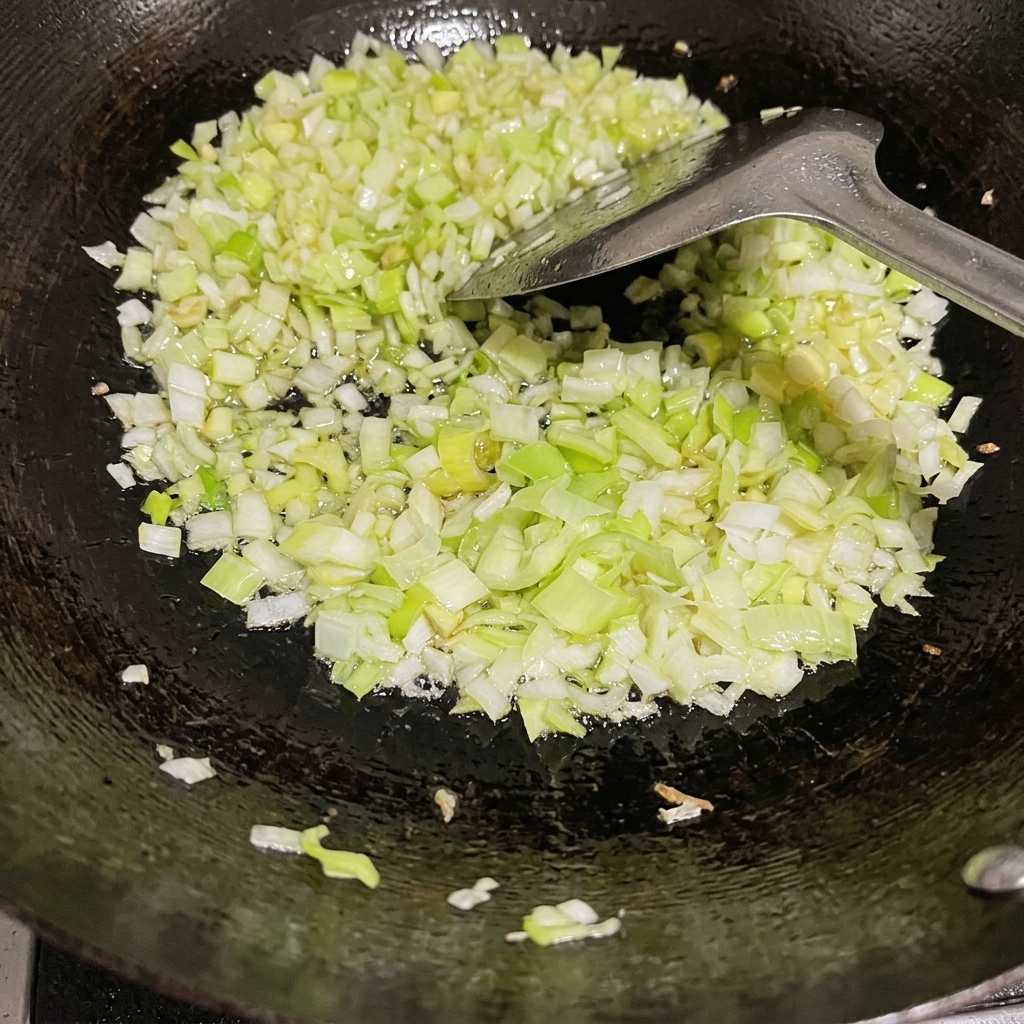 Oignons verts hachés sautant dans un wok avec un peu dhuile et une spatule en métal.