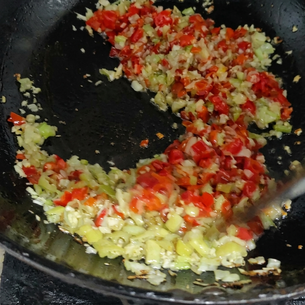 Mélange coloré de piments rouges et verts hachés sautant avec dautres aromates dans une poêle chaude.