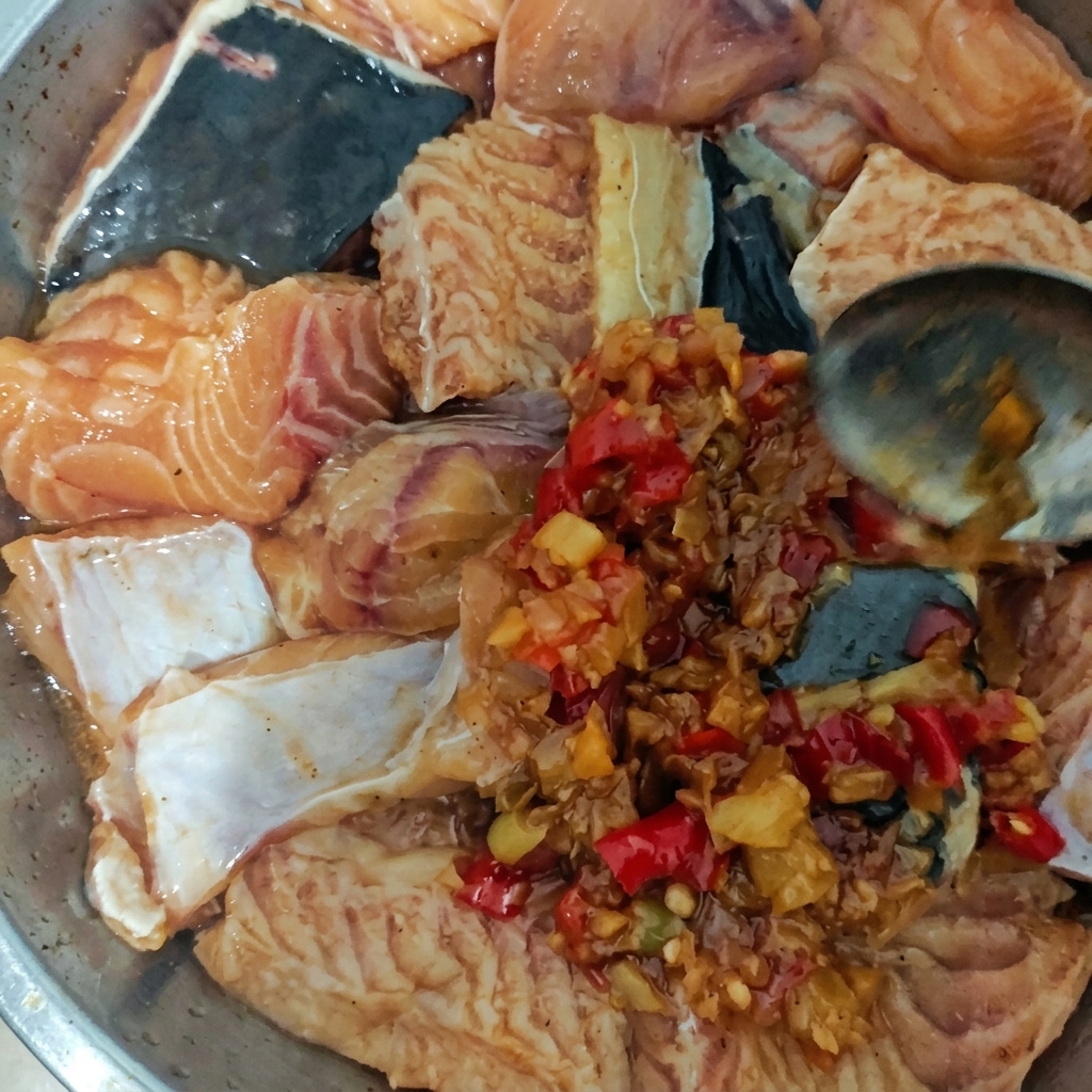 Un plat en métal rempli de morceaux de poisson cru que lon nappe dune sauce épaisse aux piments à laide dune cuillère.