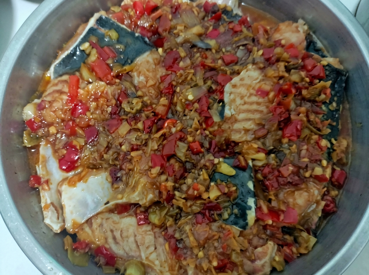 Panier vapeur en inox contenant le poisson blanc nappé dune sauce aux piments rouge vif.