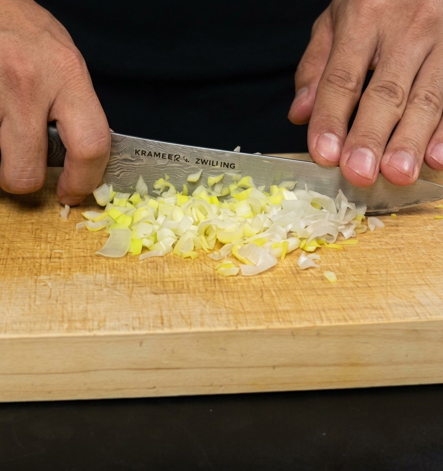 Mains utilisant un couteau de chef pour hacher finement des oignons verts sur une planche en bois.