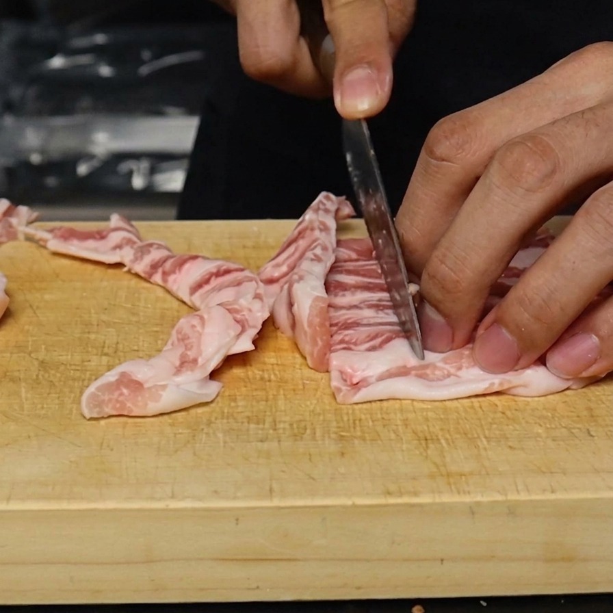 Poitrine de porc crue tranchée en lamelles régulières dun centimètre sur une planche à découper.