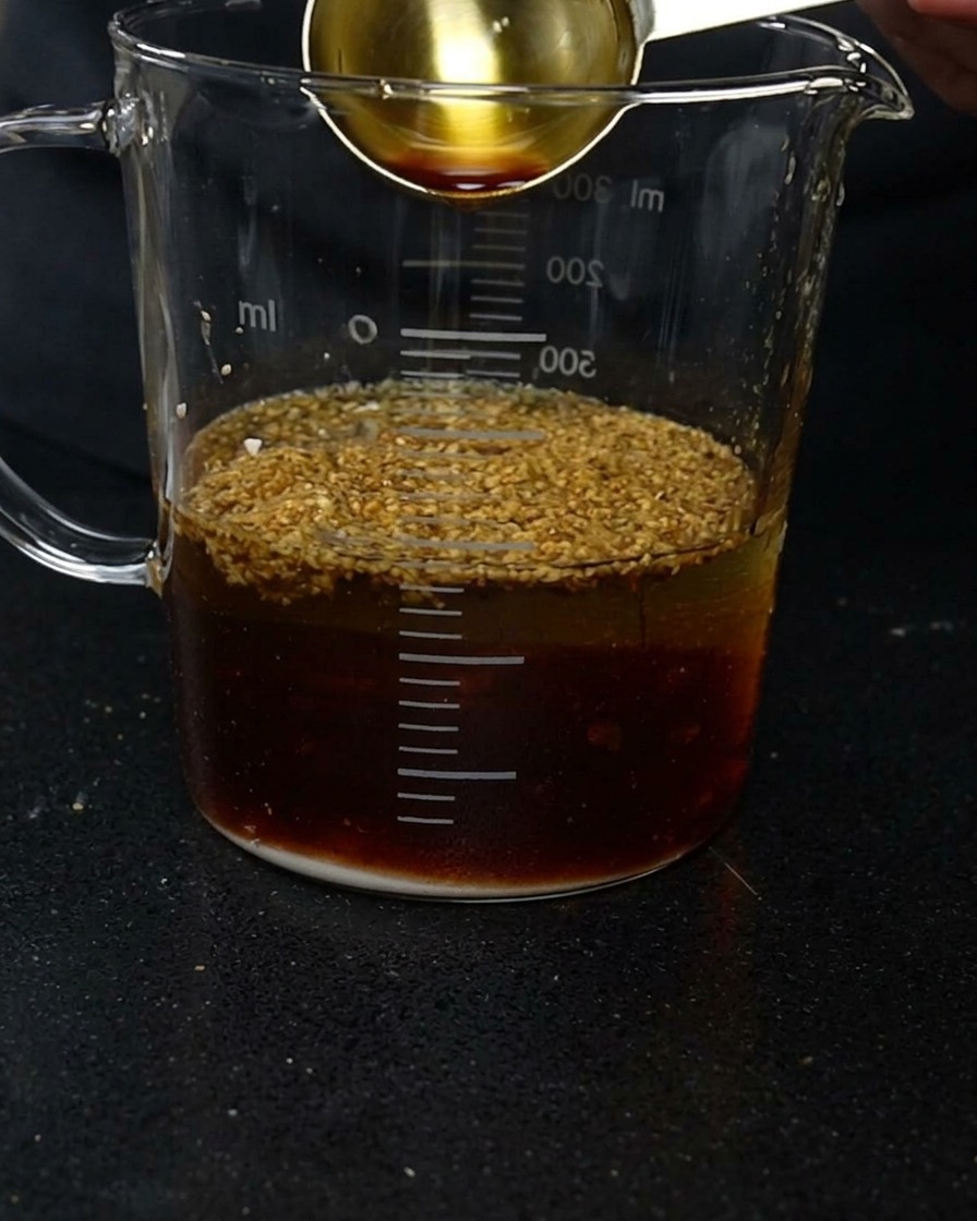 Une cuillère de mesure versant de la sauce soja dans un verre doseur contenant de leau et des assaisonnements.