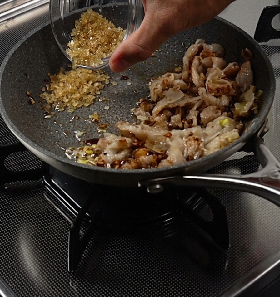 Main versant du sucre dans un espace libre de la poêle à côté du porc cuit.