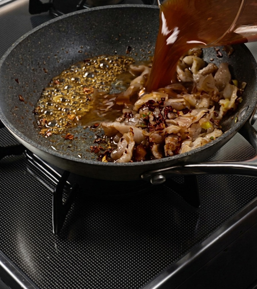 Sauce brune versée dun verre doseur dans la poêle avec le porc et le caramel bouillonnant.