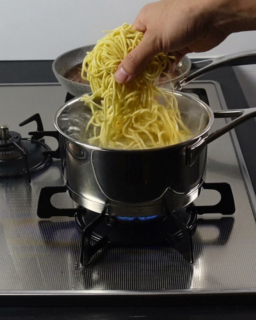 Main plongeant des nouilles ramen épaisses dans une casserole deau bouillante.