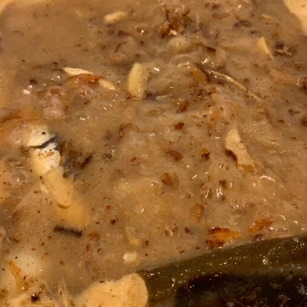 Gros plan sur les flocons de poisson et les petits poissons bouillonnant doucement dans un liquide épais de couleur beige.