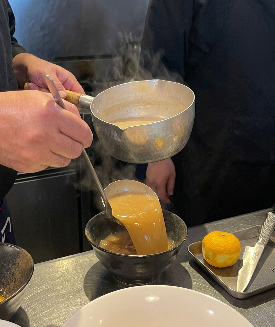 Bouillon brun épais versé à la louche dans un bol en céramique noire.