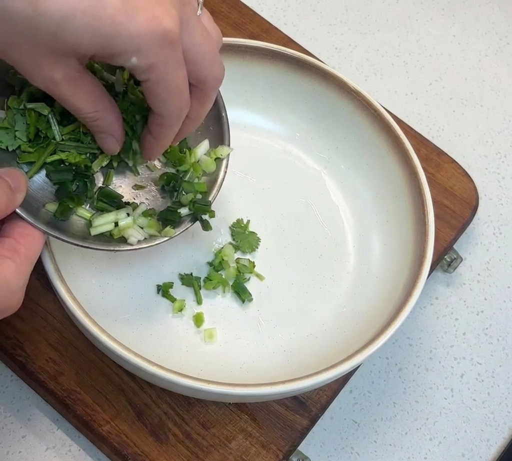 Gros plan sur des oignons verts hachés transférés dun plat en métal vers un bol blanc profond.