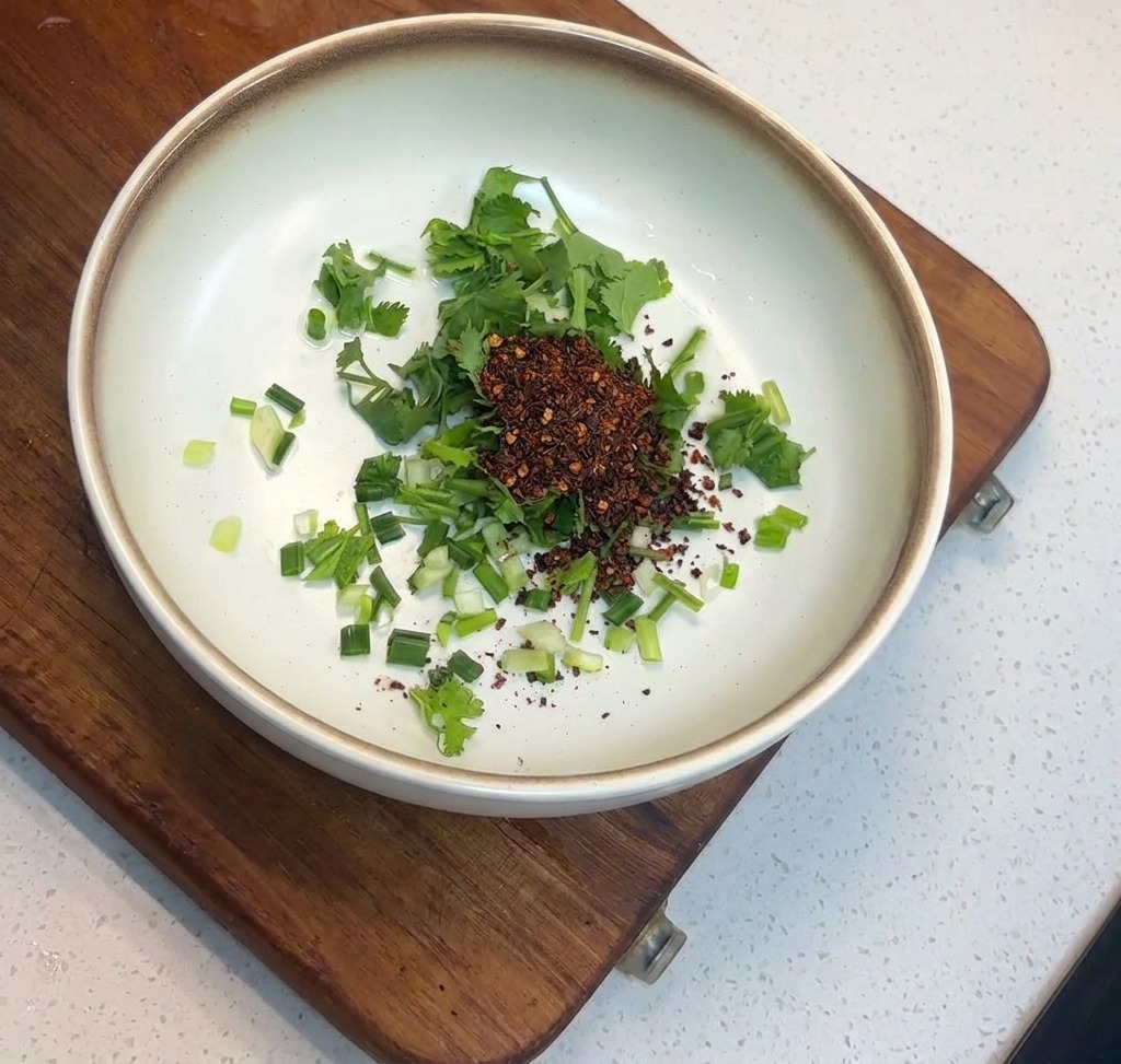 Un monticule de flocons de piment rouge foncé sur un lit dherbes vertes dans un bol en céramique.