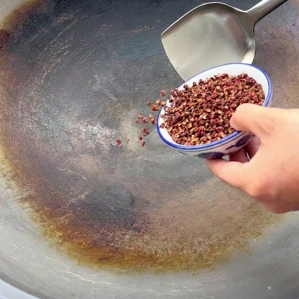 Poivre du Sichuan versé dun bol bleu et blanc dans un grand wok pour la torréfaction.