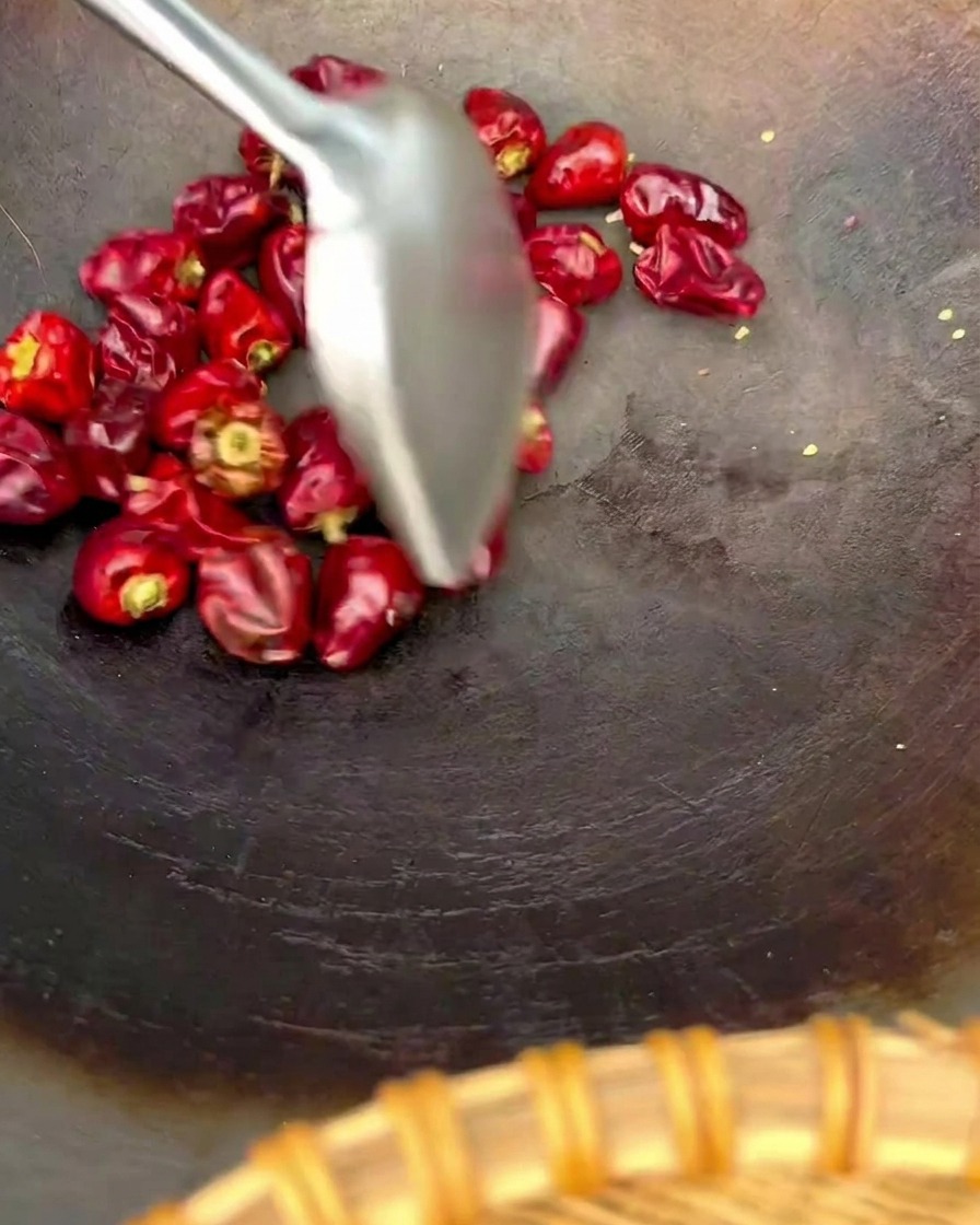 Spatule remuant des piments lanternes rouges ronds dans un wok sombre.
