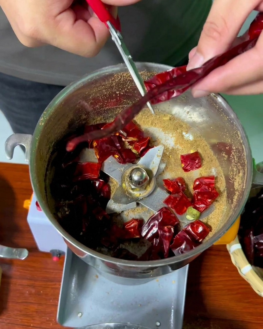 Mains utilisant des ciseaux pour couper les piments rouges séchés au-dessus du bol du moulin.